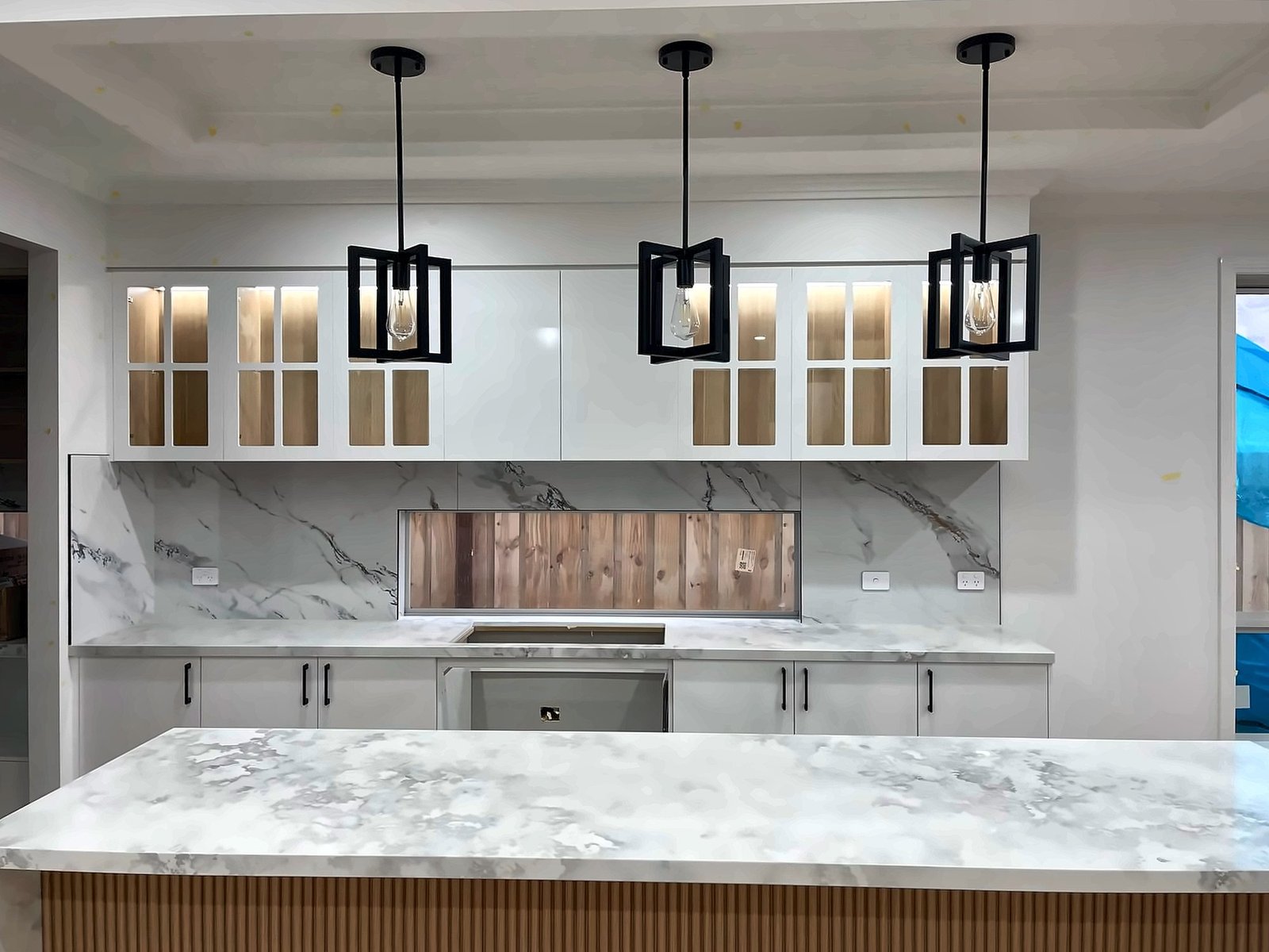 Kitchen with glass display cabinets, pendant lights and a marble-look island, by Maya Cabinets in Melbourne